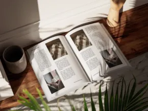 An open book and a mug on a floor, bathed in sunlight beside a potted plant, creating a cozy reading nook atmosphere. - PSD Mockup