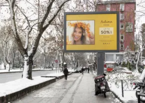 A winter city scene with a smiling woman featured on a mockup street advertisement, as pedestrians walk on a snow-lined sidewalk. - PSD Mockup
