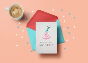 A mockup greeting card with a floral design beside a teal envelope and a coffee cup, all arranged on a pastel pink background with blue confetti. - PSD Mockup