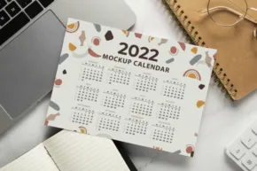 A 2022 desktop calendar template next to a laptop and office supplies. - PSD Mockup
