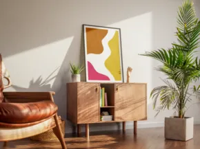 Modern living room corner template featuring a brown leather armchair, wooden cabinet displaying books and decorative items, and a colorful abstract painting. A potted palm adds a touch of greenery. - PSD Mockup