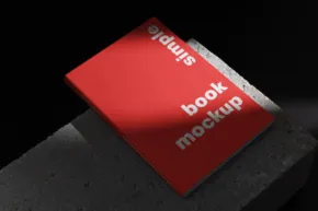 Red book template with "book mockup" text, resting on a dark textured surface, highlighted by a soft light. - PSD Mockup