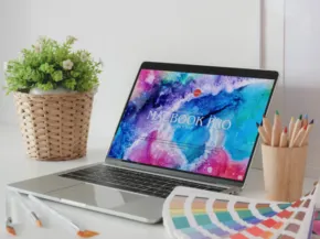 A laptop with a colorful abstract wallpaper on the screen, placed on a desk next to a potted plant and pencils, with color swatches nearby serves as an ideal template. - PSD Mockup