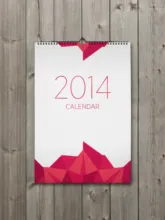 A 2014 calendar template with a geometric design, hanging on a wooden wall. - PSD Mockup