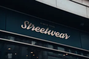 A dark storefront mockup featuring a sign reading "streetwear" in elegant, gold lettering against a gloomy building facade. - PSD Mockup