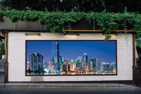 A large billboard mockup displaying a city skyline at night, set against a lush, overgrown hedge. - PSD Mockup
