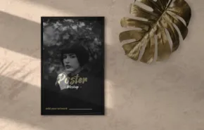 A poster template featuring a black-and-white image of a woman surrounded by flowers, titled "paradise," lies on a sunlit floor next to a gold monstera leaf. - PSD Mockup