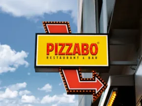 A vibrant pizzabo signboard in red and yellow mounted on the side of a building with a clear blue sky in the background serves as an ideal template. - PSD Mockup