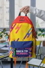 Person holding a colorful "back to school" backpack in a classroom setting as a mockup. - PSD Mockup