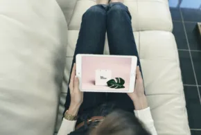 A woman holding an ipad mockup while sitting on a couch. - PSD Mockup
