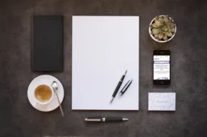 A white paper with pens and a cup of coffee on a table mockup. - PSD Mockup