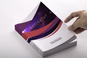 A hand is holding a book with a purple and red design, creating a realistic mockup. - PSD Mockup