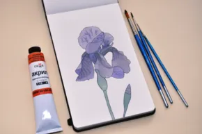 A purple iris on a notebook next to paints and brushes. - PSD Mockup