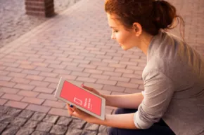 A woman sitting on the sidewalk with a tablet, creating a mockup. - PSD Mockup