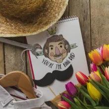 A notebook, hat, tulips, and a mustache on a wooden table mockup. - PSD Mockup