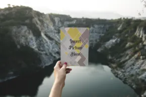 A person holding up a card in front of a cliff, serving as a mockup. - PSD Mockup
