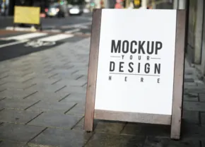 A sign mockup on a sidewalk in front of a building, a perfect template for designing. - PSD Mockup