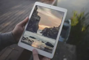 A person holding up a mockup of an iPad with a picture of a lake. - PSD Mockup