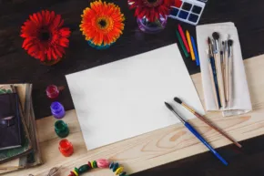 Art supplies on a table with a white sheet of paper, creating a template for artwork. - PSD Mockup