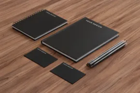 A set of black notebooks and pens on a wooden table. - PSD Mockup
