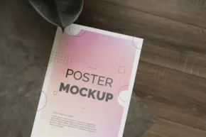 A poster mockup template on a table next to a plant. - PSD Mockup