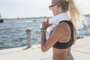 A woman wearing a sports bra and running shorts near a body of water showcases a template for fitness enthusiasts. - PSD Mockup